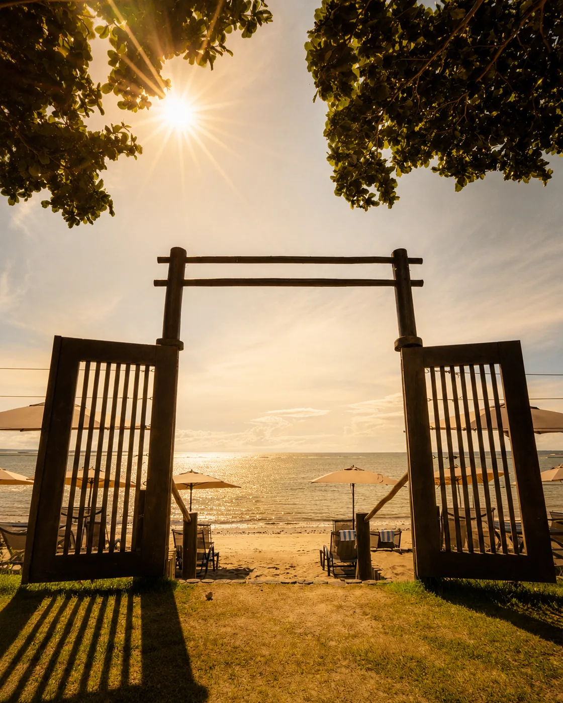 Portal de madeira na areia da praia de Arraial d'Ajuda, com o mar ao fundo