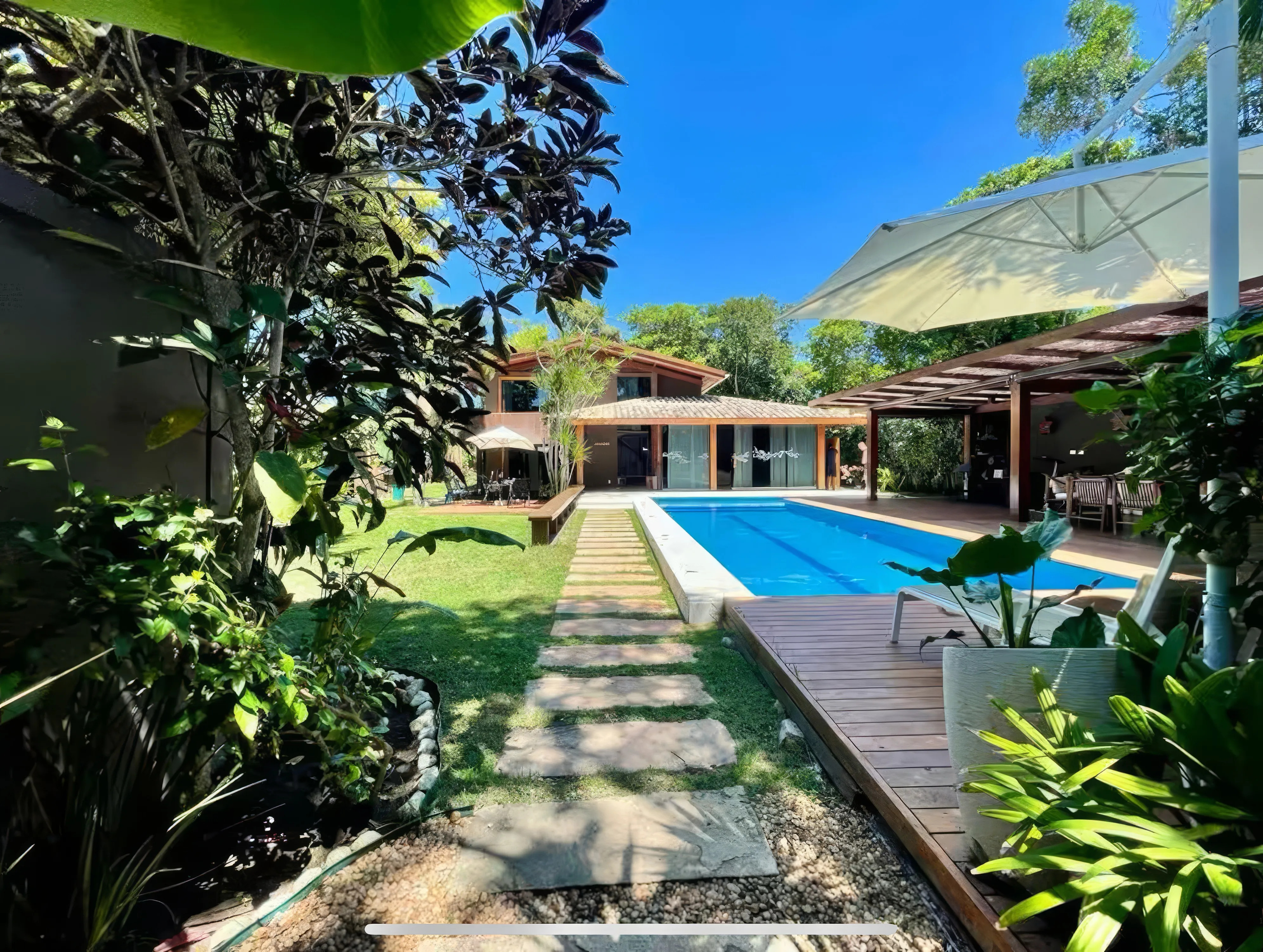 Vista da área externa da Casa Paraíso com piscina e jardim tropical.